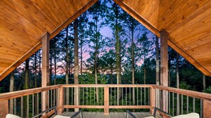 Une terrasse en bois offrant une vue sur de grands arbres et un coucher de soleil.