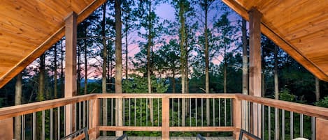 Una terraza de madera con vistas a altos árboles y un atardecer.