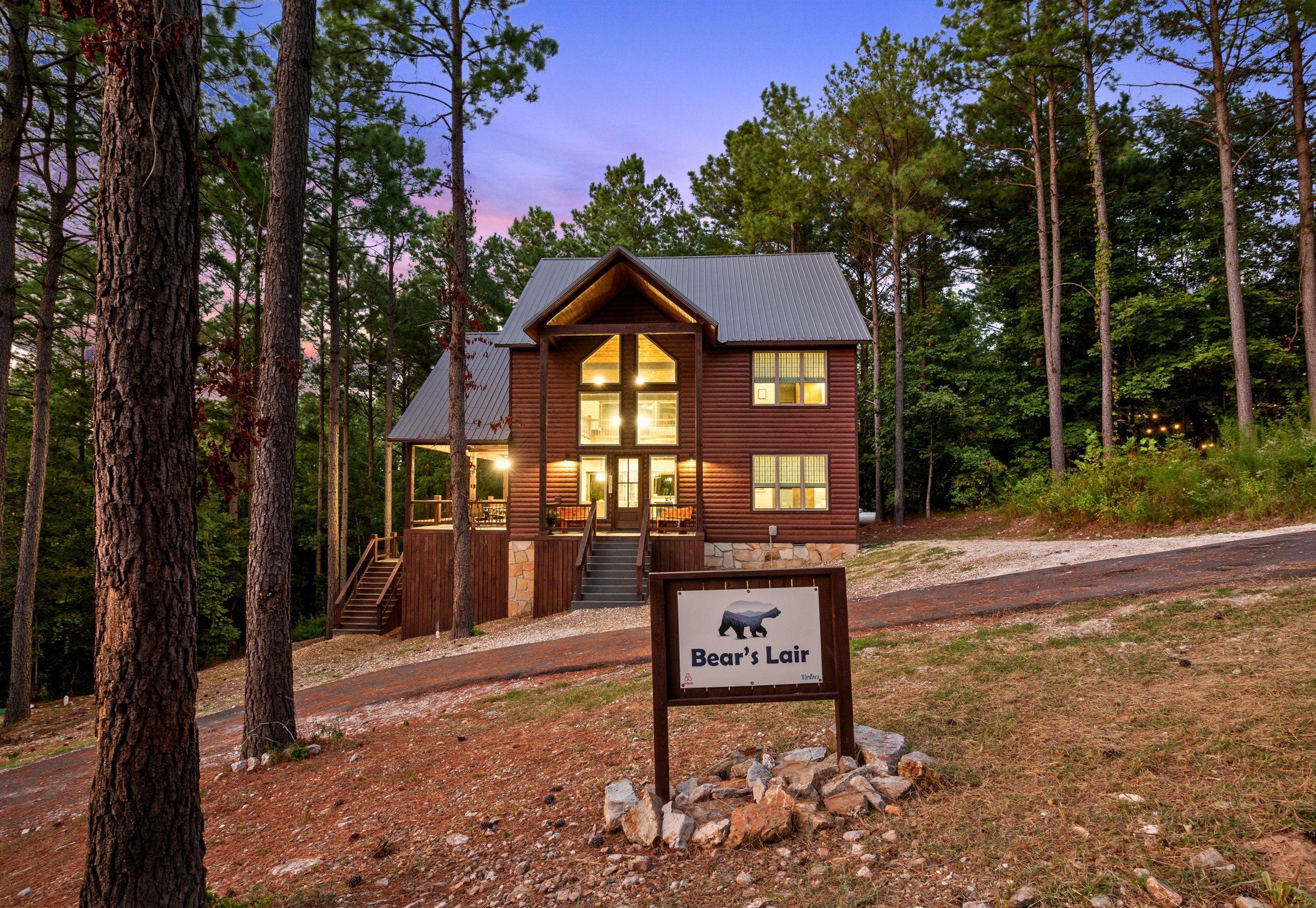 A lodge with a stone staircase leading to a wooden deck, surrounded by tall pine trees.