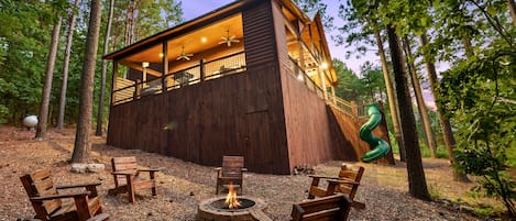 A cabin with a fire pit and outdoor seating, surrounded by trees.