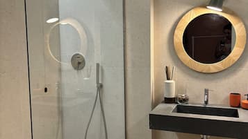 A modern bathroom with a glass-enclosed shower, a round mirror with a wooden frame, and a black sink with a chrome faucet.