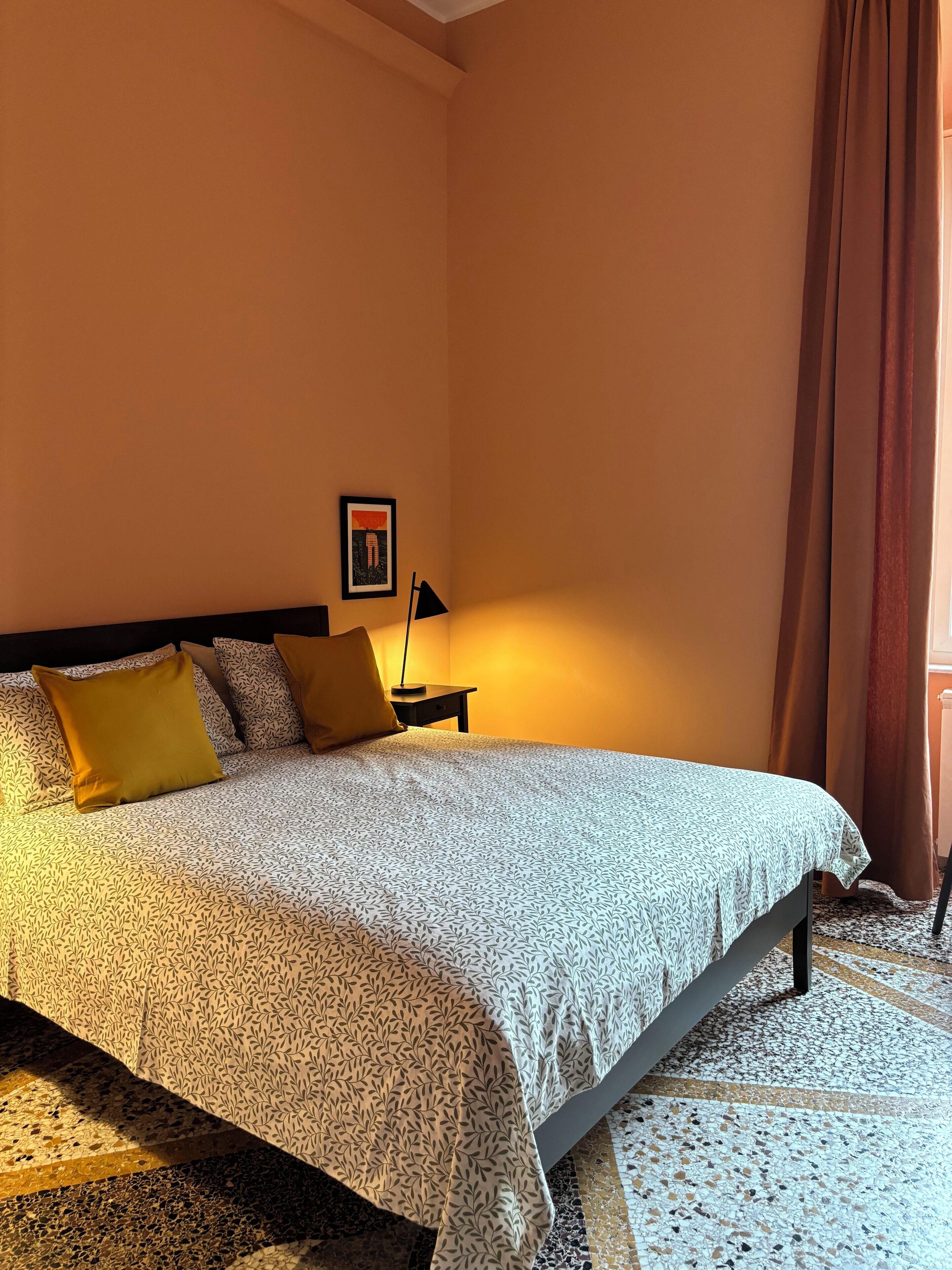 A bedroom with a bed, pillows, a nightstand, a lamp, and a framed picture on the wall.