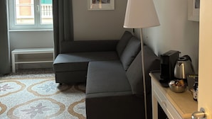 A modern room with a grey sofa, a bedside table with a lamp, a coffee maker, and a picture on the wall. - B&B Genova Holiday (Genoa)