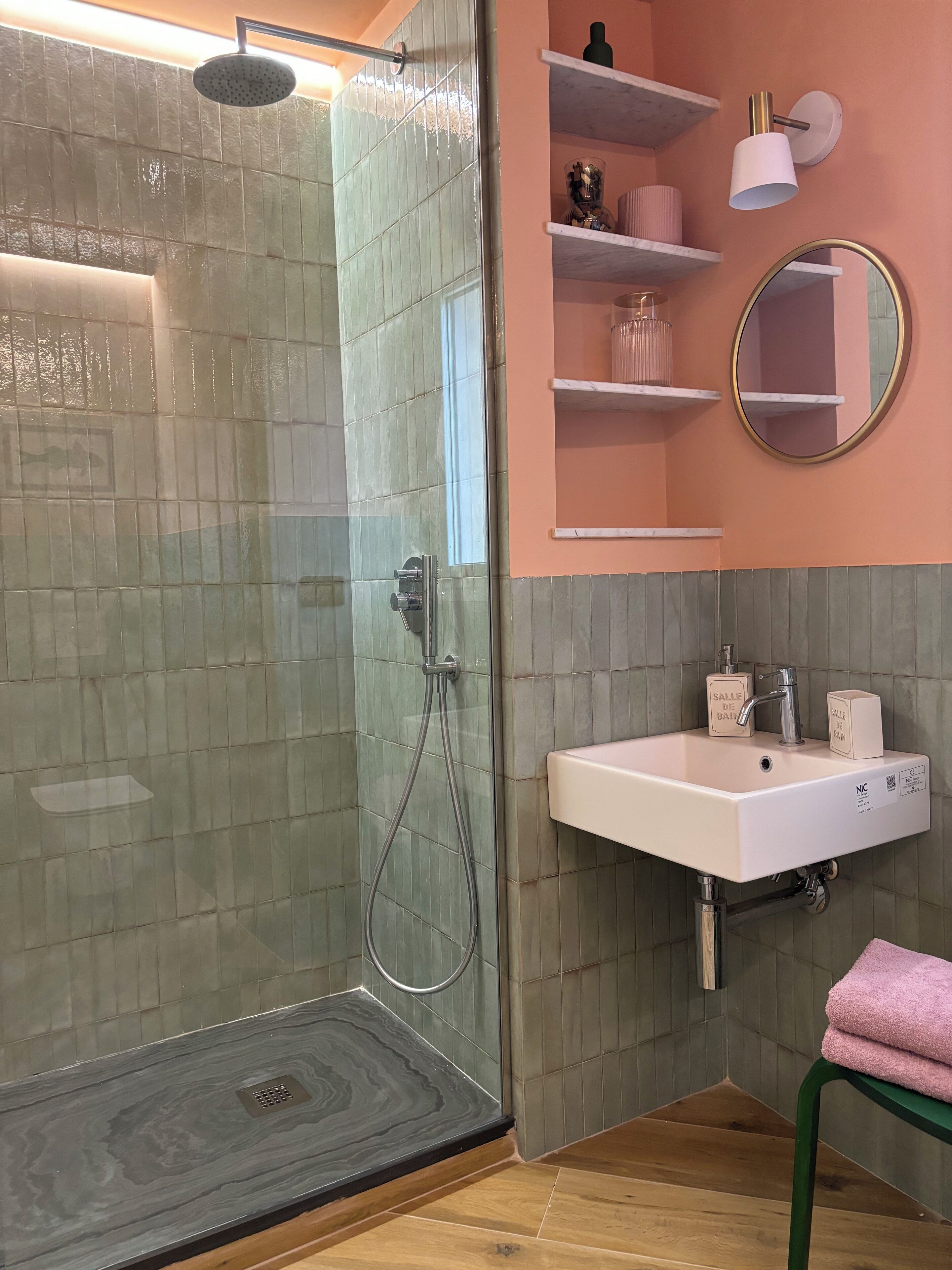 Une salle de bain avec une douche à parois de verre, un lavabo blanc avec un miroir et des serviettes roses.