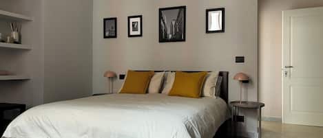 Un dormitorio con cama, dos mesitas de noche, una puerta y tres cuadros enmarcados en la pared.