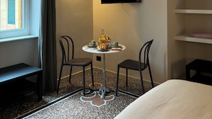 A hotel room with a bed, a small round table with a bottle, cups, and a book, two chairs, a TV mounted on the wall, and a window with curtains. - B&B Genova Holiday (Genoa)