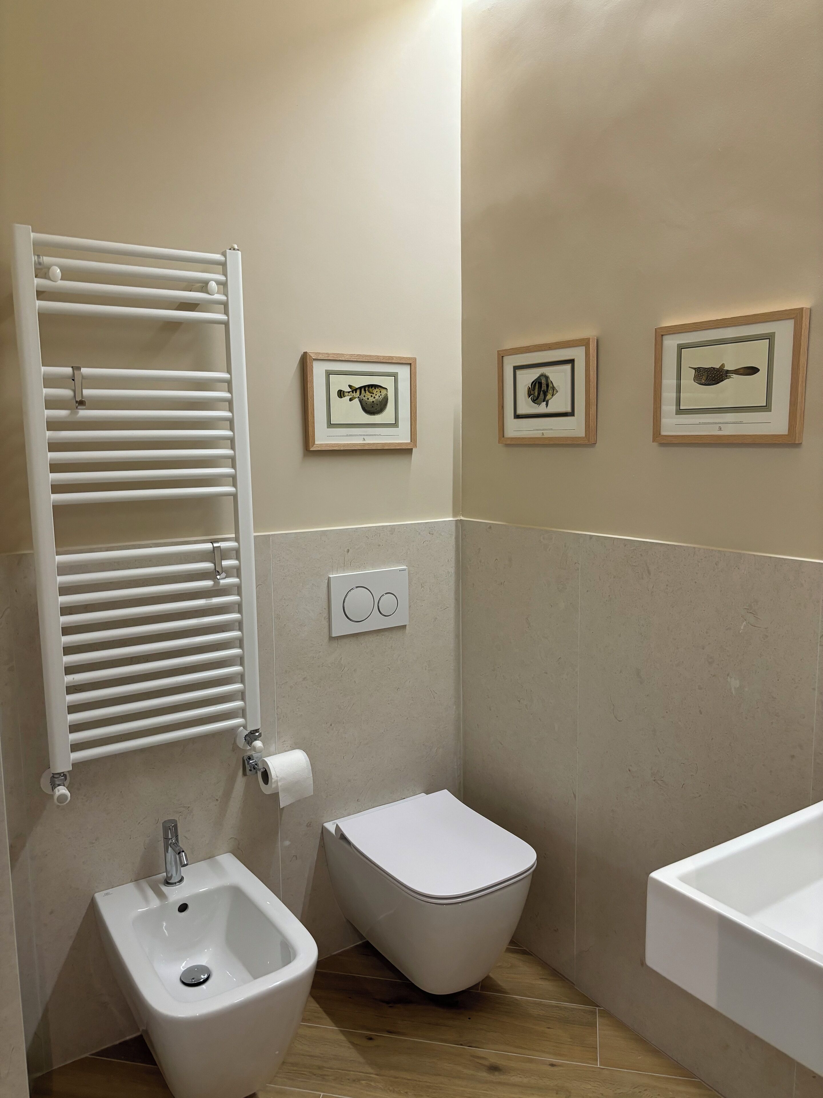Une salle de bain équipée d’un bidet, de toilettes, d’un lavabo, d’un porte-serviettes et de tableaux encadrés au mur.