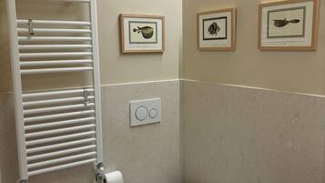 A bathroom with a bidet, toilet, sink, towel rack, and framed pictures on the wall.