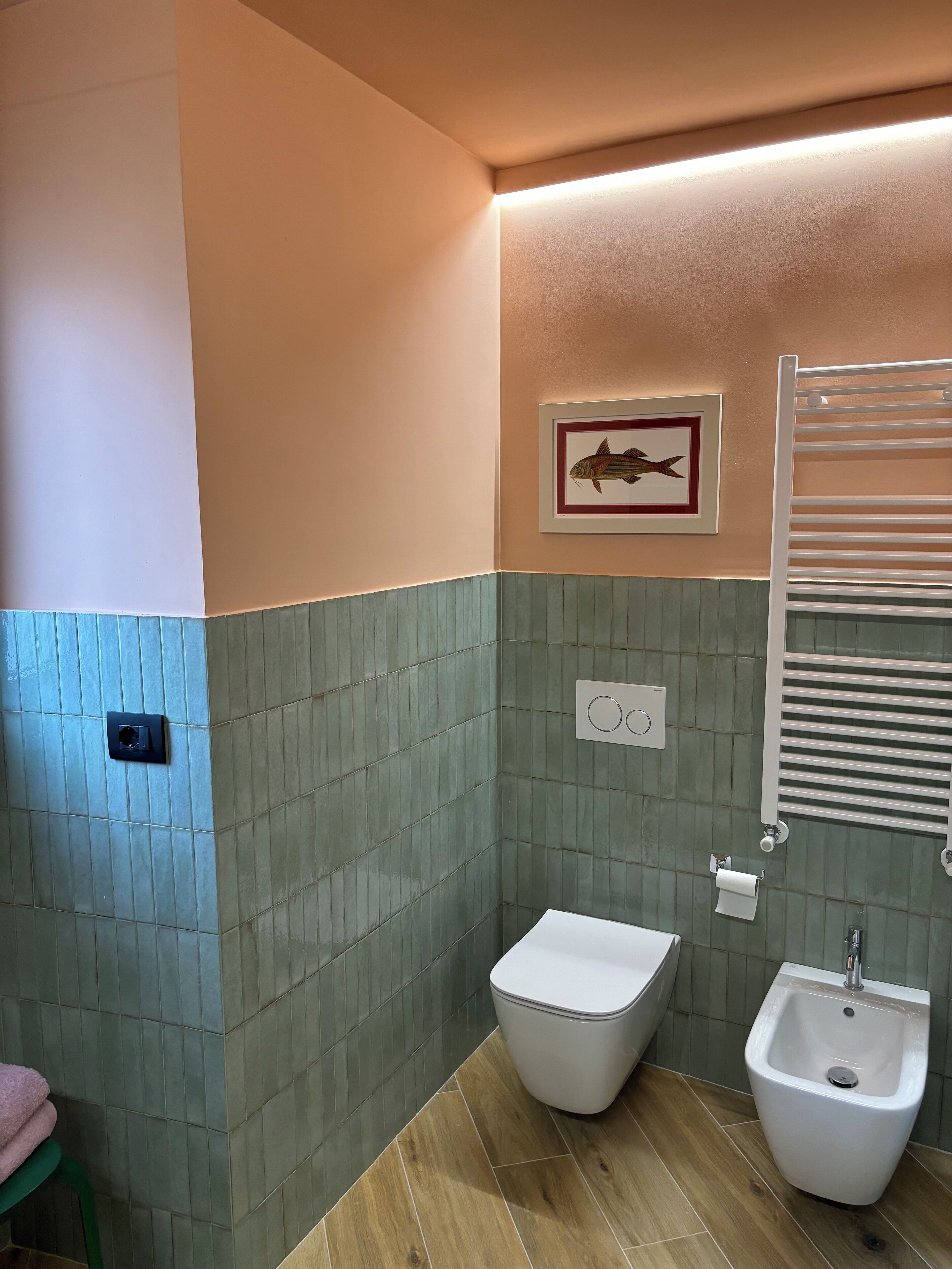 Un baño con bidé, un perchero y un cuadro de un pez en la pared.
