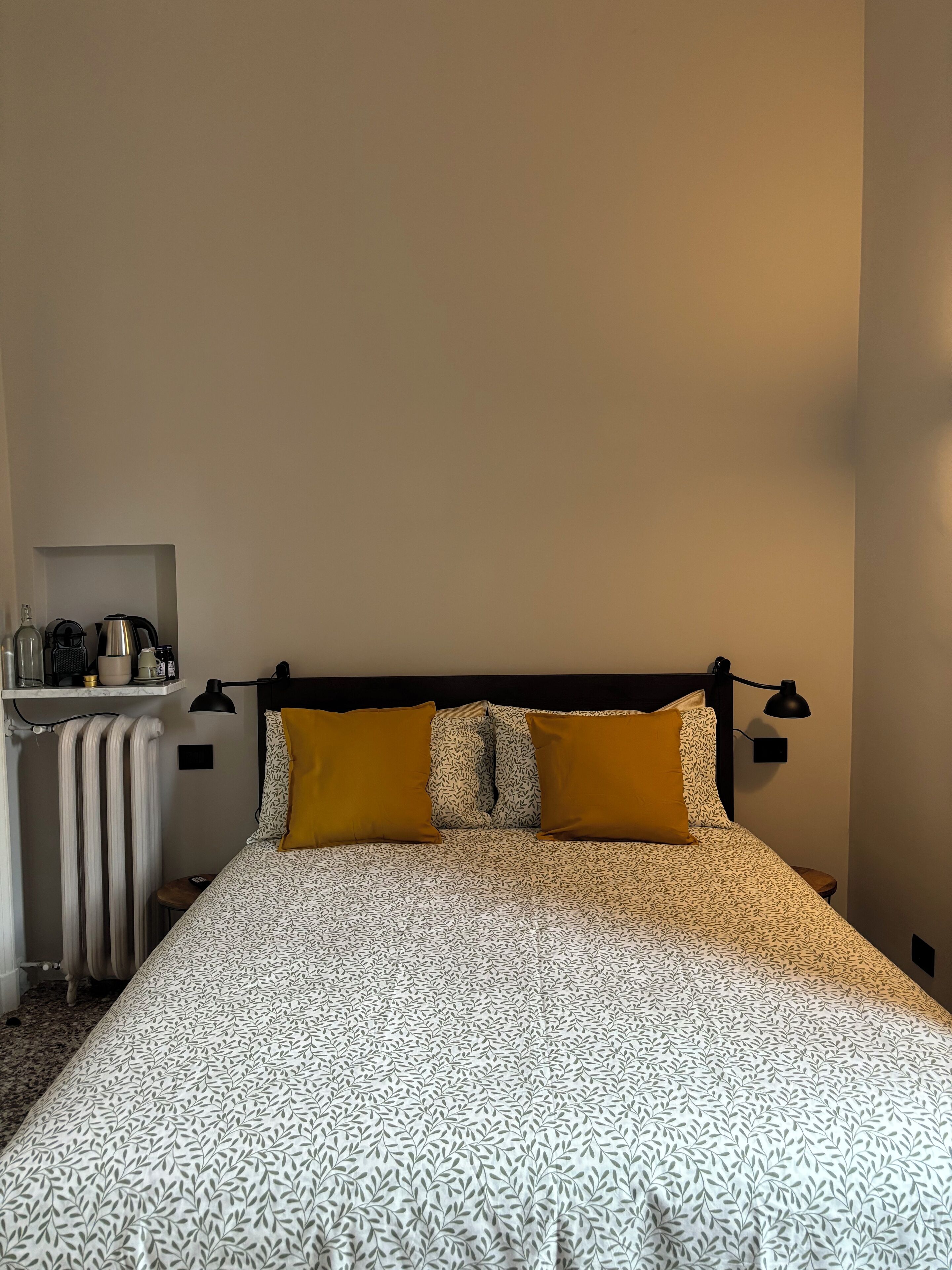 Una cama bien hecha con ropa de cama estampada, una mesita de noche con una lámpara y un radiador.