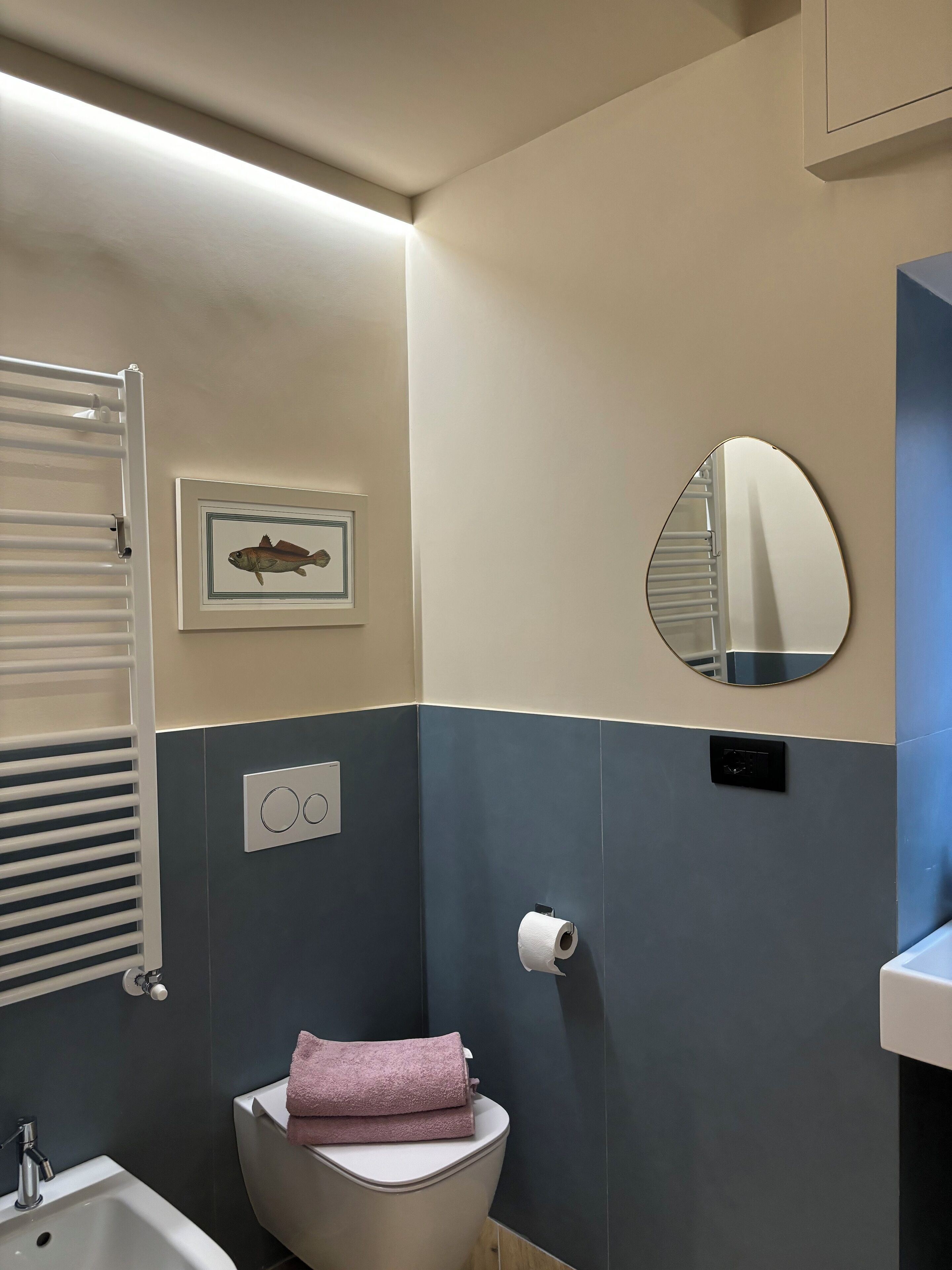 A bathroom with a toilet, a sink, a towel, a framed fish picture, a mirror, and a toilet paper holder.