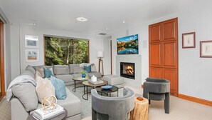 A modern living room with a fireplace, grey sofas, and a television mounted above it. - Liftside C22 | Ski-In/Ski-Out 3BR at Cascade Village (Vail)