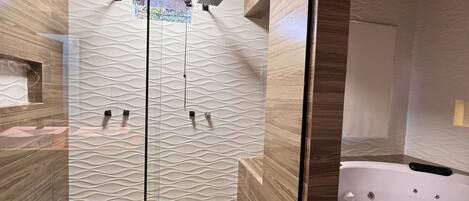 A modern bathroom with a glass-enclosed shower, wooden flooring, and a built-in bathtub.