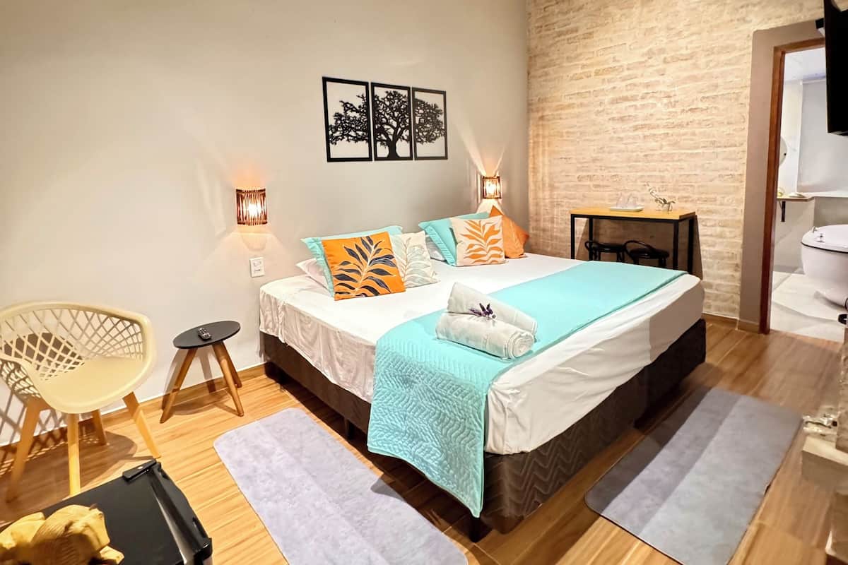 Une chambre avec un plafond en bois, un lit recouvert d’une couverture bleue, une petite table avec une lampe et une chaise.