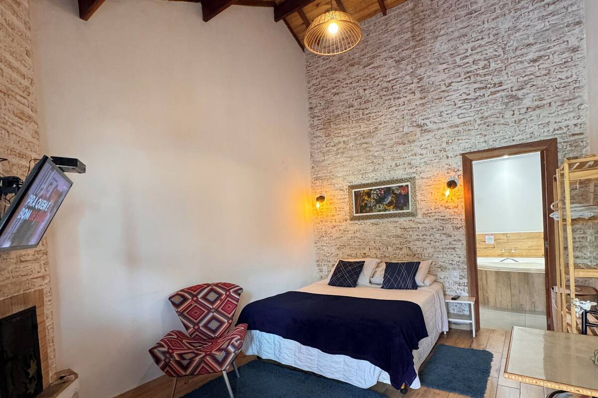 Une pièce confortable avec un lit, une chaise, une table et une cheminée.