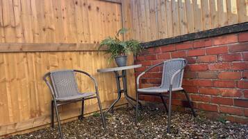 Een terras met twee rieten stoelen, een bijzettafeltje en een plant in een pot.
