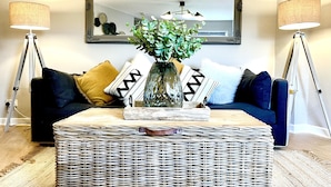 A living room with a dark blue sofa, a wicker coffee table, and two floor lamps. - Central Ellesmere -sleeps2 - Parking - Petfriendly (Ellesmere)