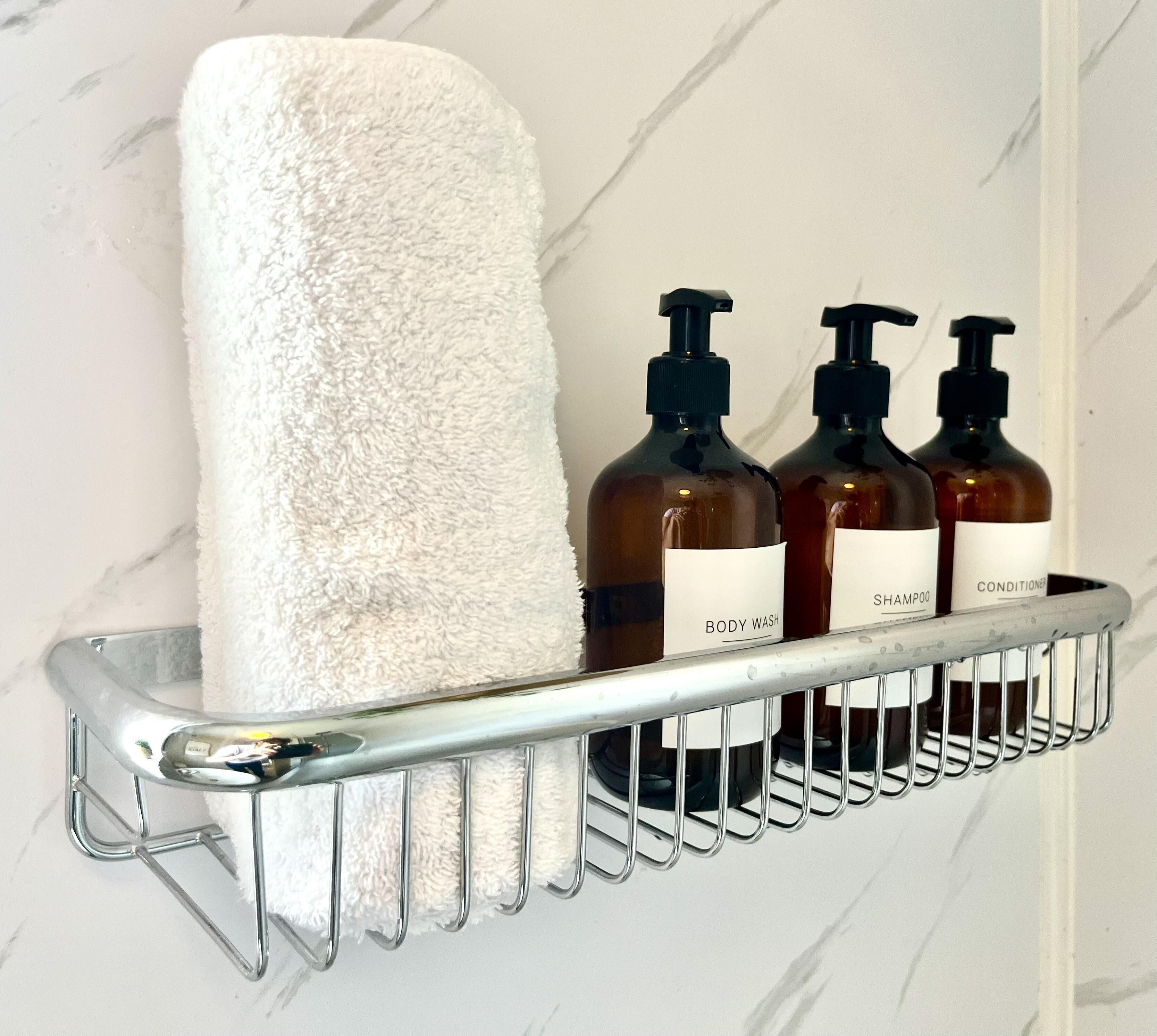 A bathroom shelf with a white towel and three bottles labeled body wash, shampoo, and conditioner.