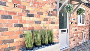 A brick wall with a wooden planter box containing tall green plants. - Central Ellesmere -sleeps2 - Parking - Petfriendly (Ellesmere)