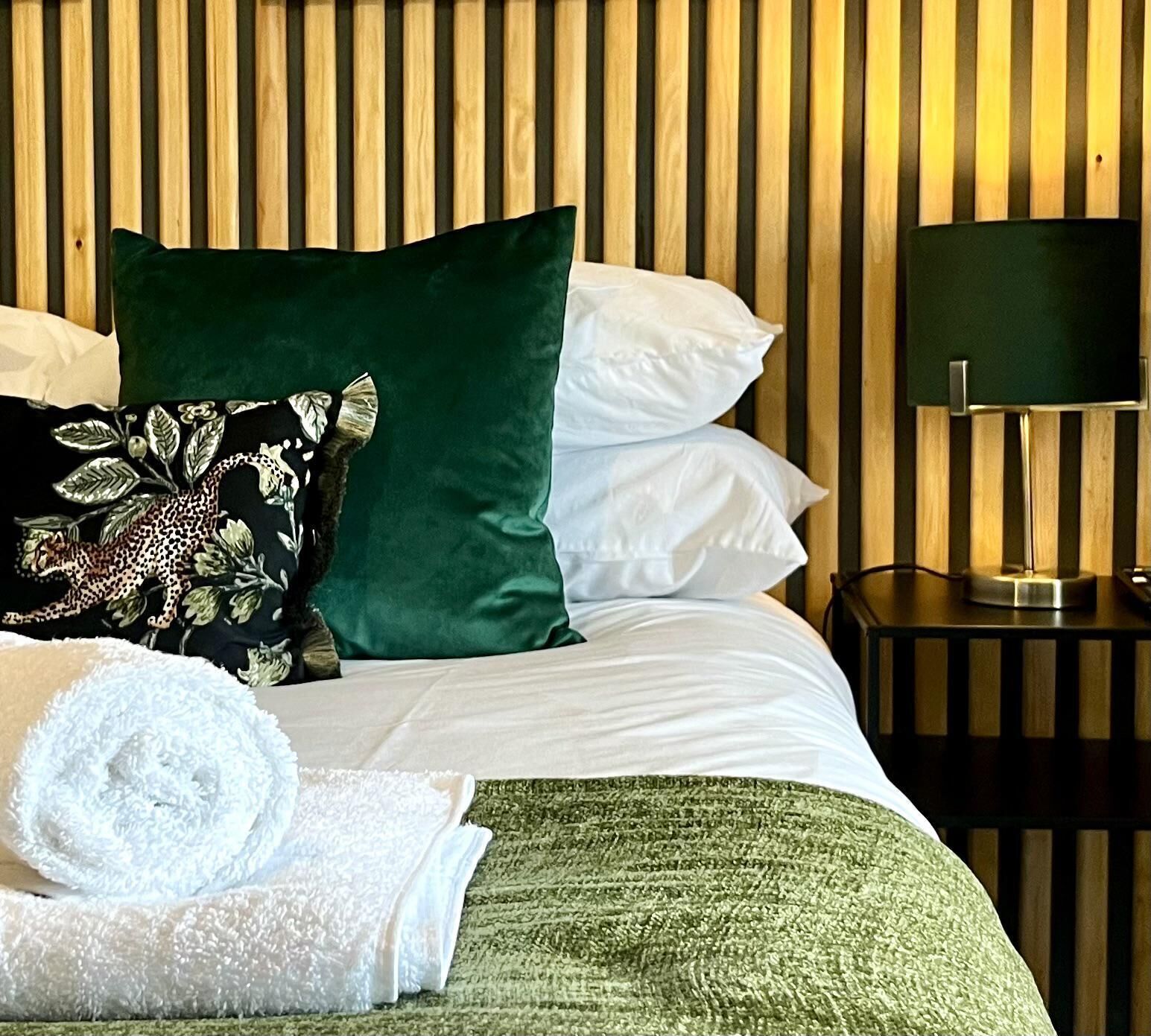 A neatly made bed with white and green bedding, a floral pillow, and a green throw blanket.