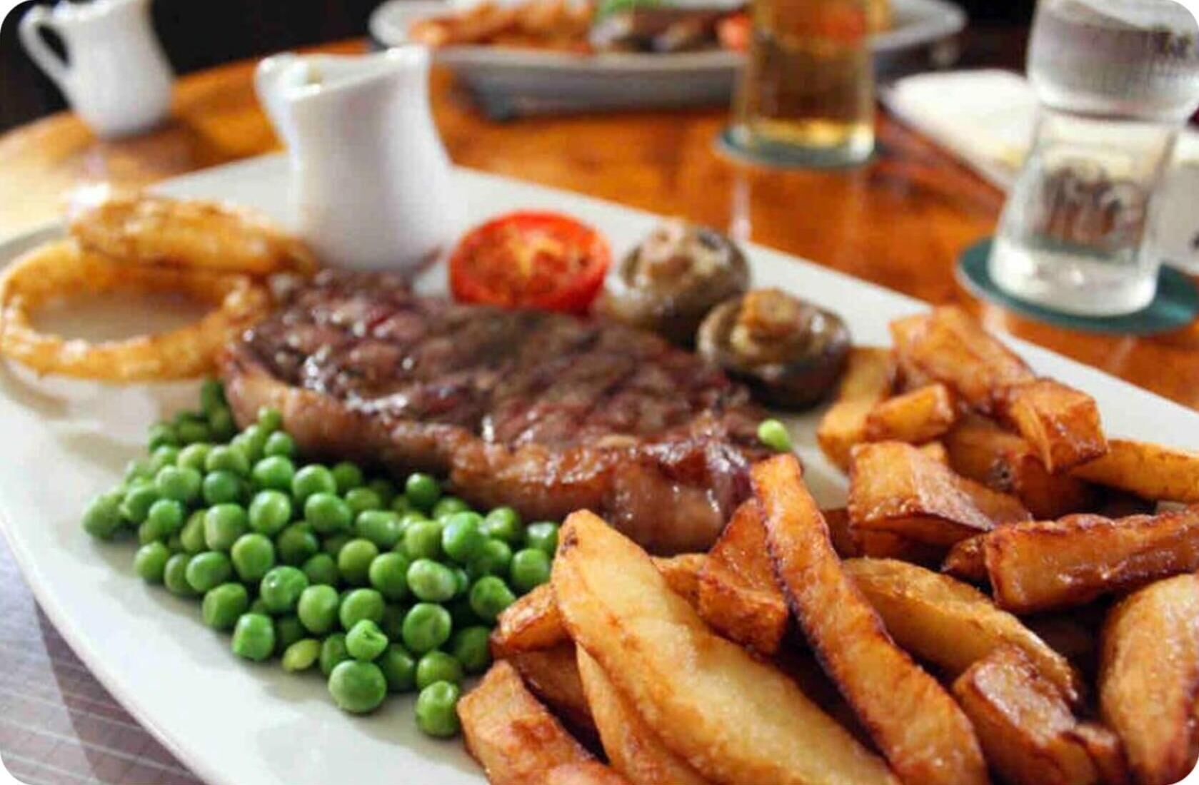 A plate with steak, fries, peas, onion rings, and mushrooms.
