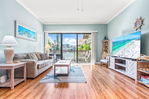 A living room with a sofa, coffee table, TV, and a view of the beach through the balcony.