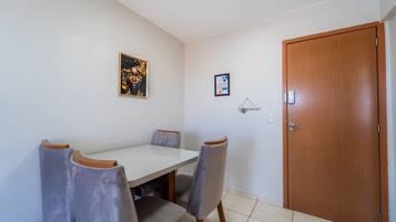 Uma área de refeições com uma mesa branca e quatro cadeiras, uma porta de madeira e dois quadros na parede.