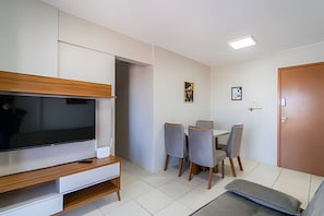 A modern living room with a flat-screen TV, wooden entertainment unit, grey dining chairs, and a small table.