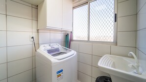 A laundry room with a front-loading washing machine, a sink, and a window with a metal grid.