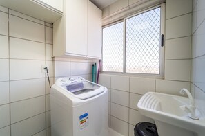 A laundry room with a front-loading washing machine, a sink, and a window with a metal grid.