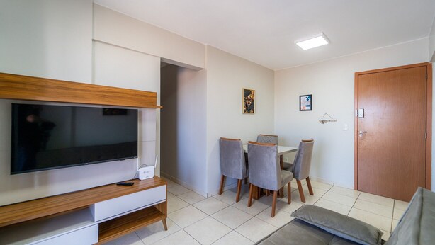 A living room with a flat-screen TV, a wooden entertainment unit, a dining table with chairs, a sofa, and a door.