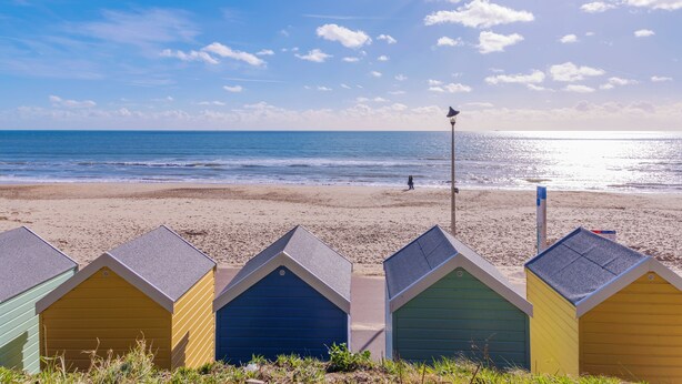 Beach huts with a view of the sea and a person walking on the beach. - St Michael's Holiday Home (Bournemouth)