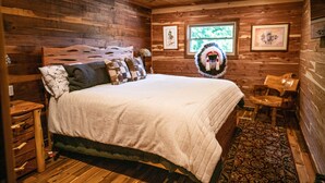 Ein Schlafzimmer einer Holzhütte mit Bett, Holz-Kopfteil, Deckenventilator und Teppich.