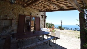 A stone building with a wooden table and benches, a stone fireplace, and a view of the sea. - Villa Roccella Ionica, Sea View, a c (Roccella Ionica)