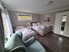 A bedroom with two beds, a window, a bedside table with a lamp, a wardrobe, and a chair.