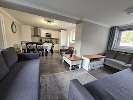 A modern living room with grey sofas, a wooden coffee table, and a dining area with a white table and chairs.