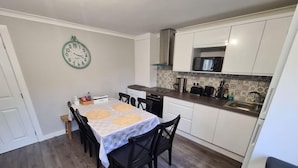 Una cocina compacta con zona de comedor, que incluye un reloj en la pared, un microondas y un fregadero.