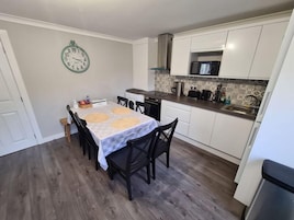 A compact kitchen with a dining area, featuring a clock on the wall, a microwave, and a sink.