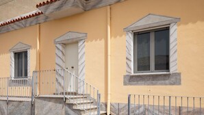 A building with a yellow facade, a tiled roof, and a staircase leading to a door. - Casa Bata by Wonderful Italy (Budoni)