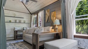 Ett mysigt rum med en soffa, en pall och ett bord med en lampa. Det finns hyllor med dekorativa föremål och ett fönster med gardiner.
