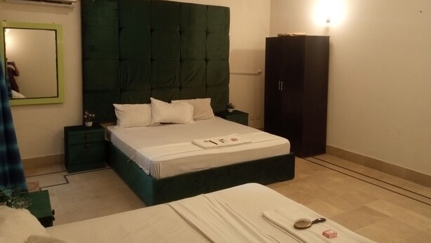 Een slaapkamer met een groot bed, een donkergroen hoofdeinde, een kledingkast, een nachtkastje en een plafondventilator.