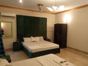 Una camera da letto con un letto grande, una testiera verde scuro, un armadio, un comodino e una ventola a soffitto.