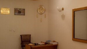 Een kamer met een plafondventilator, een bureau met papieren, een stoel, een wandklok en een lijst met een afbeelding.