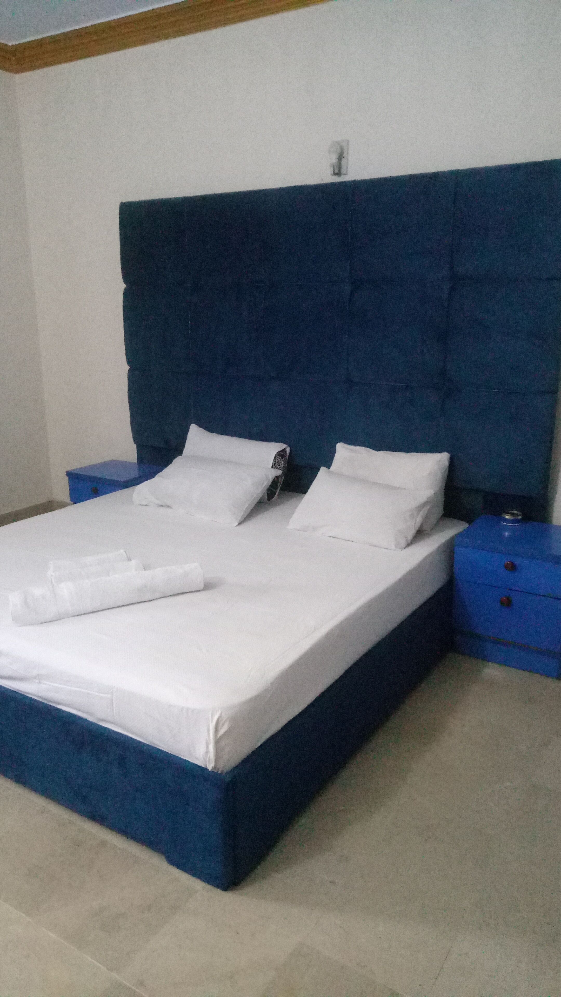 A bed with a blue headboard, white bedding, and two nightstands with drawers.
