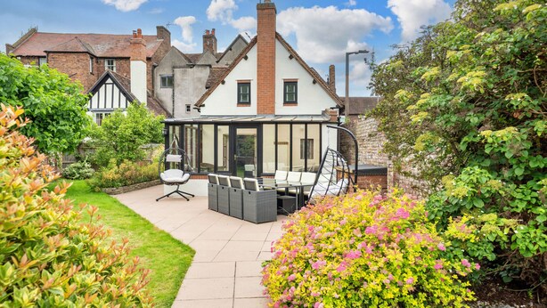 A traditional house with a conservatory, a patio with outdoor furniture, and a well-maintained garden. - Barn Cottage (Bridgnorth)