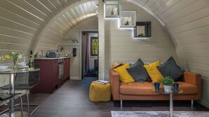 Une cuisine moderne avec un plafond incurvé, un coin repas avec une table et des chaises en verre, et un espace de vie confortable avec un canapé et des coussins.