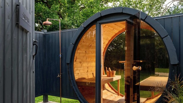 Une structure circulaire en bois, dotée d’une porte en verre, d  ’une terrasse en bois et d’un petit espace extérieur aménagé avec une table et des chaises.