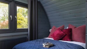 Une chambre à coucher avec une couvre-lit bleu foncé, des coussins rouges et une fenêtre donnant sur des arbres.