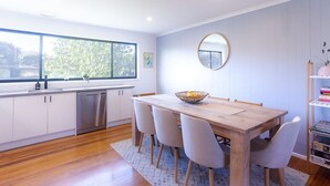 A modern kitchen with white cabinets, a wooden dining table, and a large window. - 428 Eastbourne Road · Rosebud Garden Cottage (Capel Sound)