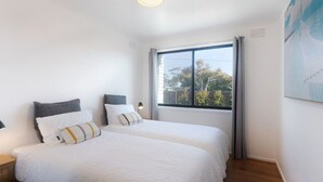 A double bed with white bedding and two pillows, a bedside table, a window with curtains, and a ceiling light. - 428 Eastbourne Road · Rosebud Garden Cottage (Capel Sound)